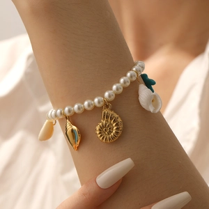 Détail d'un bracelet de perles au poignet avec des breloques marines dorées et bleues