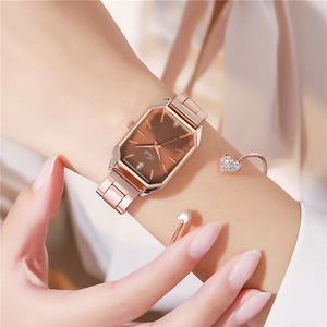 Close-up of elegant rose gold rectangular watch with brown dial worn with a heart bracelet