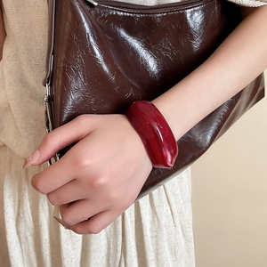 Detail of a wide red acrylic cuff bracelet with marbled texture worn by a model