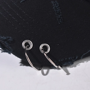 Detail of distressed black denim baseball cap with frayed edges and silver metal rings