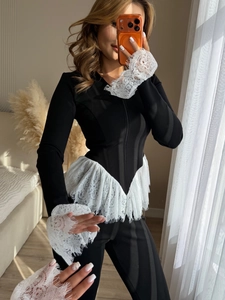 Detail eines schwarzen Cardigans mit eleganten weißen Spitzenrüschen an Manschetten