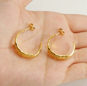 Detailed close-up of gold C-shaped earrings with hammered metal texture held in hand