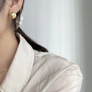 Close-up of a minimalist golden spherical stud earring worn on a model's ear