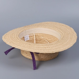 Detailed view of 100% raffia straw hat interior with wash label and purple ribbon