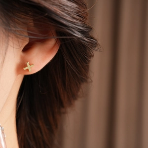 Close-up of a minimalist gold cross stud earring worn on a model's ear lobe