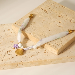 Detail of silk scarf bracelet with gold shell charms and purple beads on travertine stone