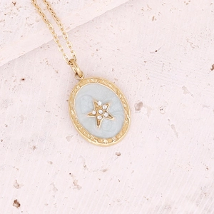 Macro detail of a gold oval pendant with light blue enamel and a central zircon star