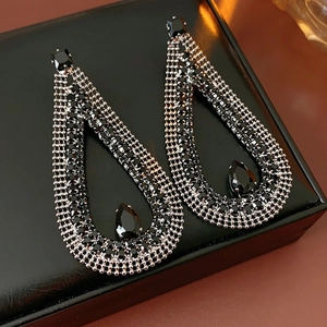 Close-up of teardrop earrings with black crystals and silver accents on a leather box