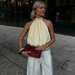 Hellgelbes Neckholder-Top mit Falten zu weißer weiter Hose und roter Clutch-Tasche