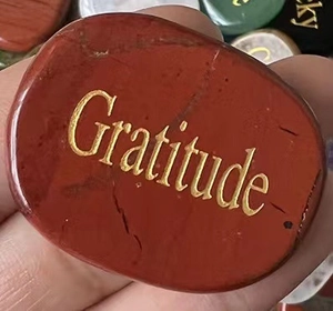 Macro shot of a red natural gratitude stone with engraved gold lettering in hand