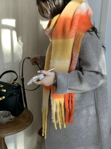 Close-up of thick knit plaid scarf in orange and yellow with long fringe tassels