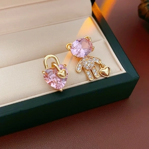 Close-up of asymmetric gold bear and pink heart zircon earrings in a premium jewelry box