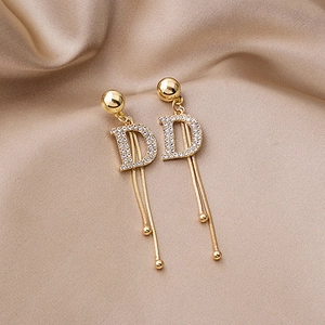 Close-up of golden tassel earrings featuring a crystal D-letter and sparkling fringe