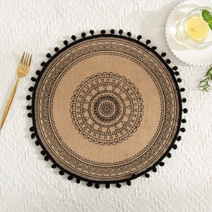 Detailed top view of a round jute placemat with black mandala pattern and fringe trim