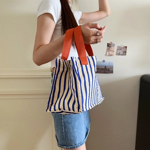 Detail of blue striped canvas tote bag featuring contrasting orange fabric handles