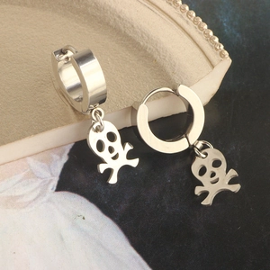 Macro detail of silver stainless steel skull charm hoop earrings on a ceramic dish