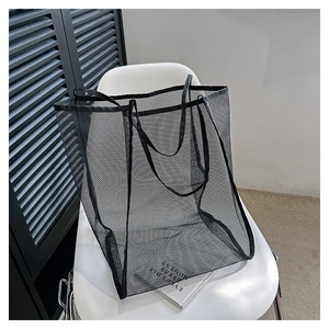 Detalle de bolso tote de malla negra con asas reforzadas sobre una silla blanca