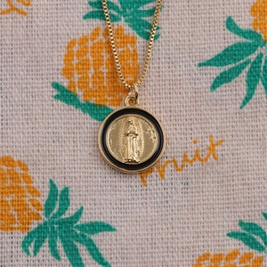 Detail of round gold pendant necklace with religious figure relief and black enamel