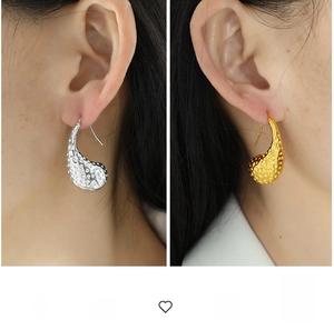 Detail view of gold and silver teardrop earrings with hammered texture on ear