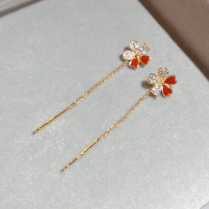 Macro shot of gold-plated flower tassel earrings with red enamel and sparkling zircons