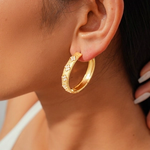 Detail of 18k gold plated hoop earring with brushed texture and clover zircon on model