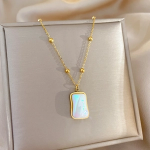 Detail of gold titanium necklace with a square rainbow mother-of-pearl pendant in a jewelry box