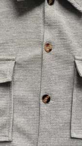 Close-up of waffle textured light gray shirt featuring resin buttons and utility pockets