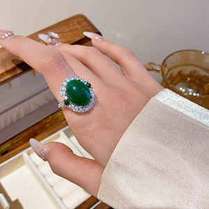 Close-up of a silver ring featuring a large oval green gemstone surrounded by white crystals