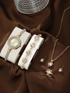Detail of gold quartz watch and heart jewelry set displayed on brown silk background