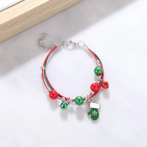 Detail of Christmas beaded bracelet with green stocking charm and red bell on marble surface