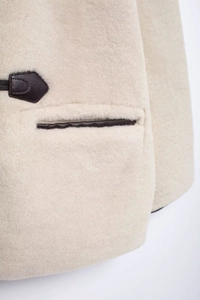 Détail d'un manteau en fausse fourrure beige avec bordures en cuir marron et coutures