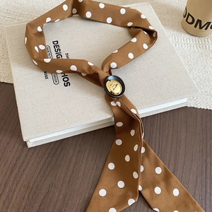 Close-up of brown polka dot silk scarf necklace with golden metal buckle on a book