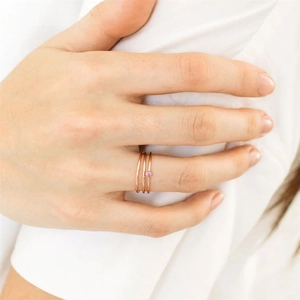 Detail shot of three rose gold titanium rings with a pink birthstone on a model's hand