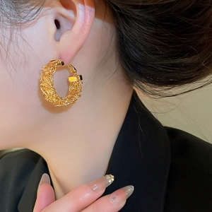 Detail of gold-plated woven texture hoop earrings worn by a model for a luxury look