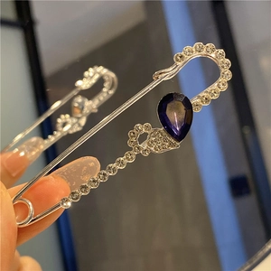Detail of silver safety pin brooch with sparkling rhinestones and blue teardrop gemstone
