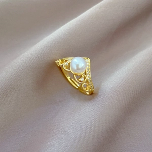 Macro detail of crown pearl ring with heart patterns and gold plating on pink silk