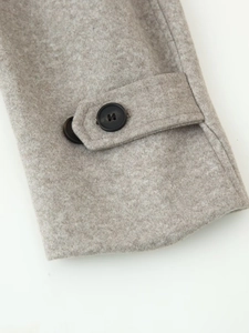 Close-up of light grey wool coat sleeve with decorative strap and dark round button