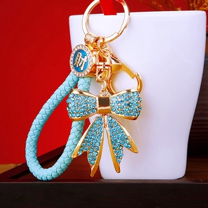 Close-up of golden bow keychain with blue rhinestones and braided leather strap detail