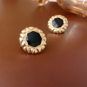 Macro shot of vintage round gold-plated earrings with black enamel and embossed texture