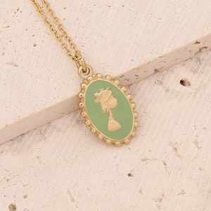 Macro shot of gold portrait pendant with light green enamel inlay on beige stone background