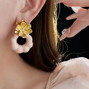 Gros plan d'une boucle d'oreille vintage fleur dorée avec anneau rose portée par un modèle