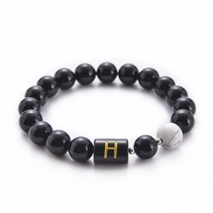 Macro shot of 10mm black onyx bead bracelet with white turquoise and gold letter H charm