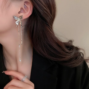 Detail of silver butterfly tassel earrings and floral ring worn by a model