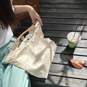 Detail of canvas tote bag showing floral bear print, orange braided handle and snap closure