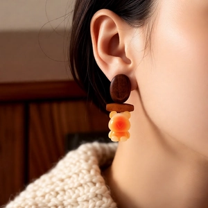 Detailed close-up of a wooden bear pendant earring worn on ear with warm knit background