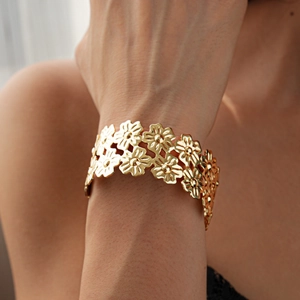 Close-up of a wide hollow floral gold bracelet on a woman wrist with metallic luster