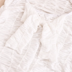 Close-up of a white halter neck dress featuring a large bow detail and ruched fabric texture