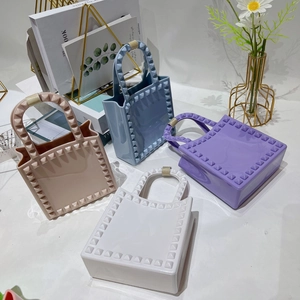 Mini PVC jelly handbags with square studs in macaron colors on a stylish white desk