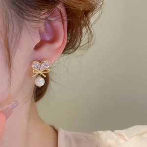 Detail of bow-shaped zircon earrings with a hanging pearl on a model's ear