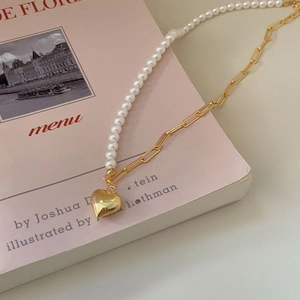 Detail view of gold heart pendant with mixed pearl and paperclip chain on a pink book